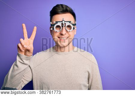 Young handsome caucasian man wearing optometrical glasses over purple background smiling with happy face winking at the camera doing victory sign. Number two.