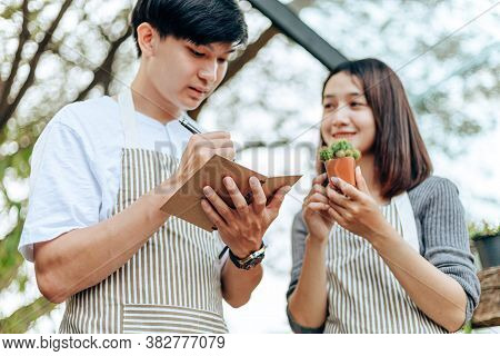 Women Hold Cactus And A Man Writing Note In A Book. Love Couple Enjoy Hobby With Darden Cactus.