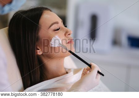 Hands Of Cosmetology Specialist Applying White Facial Mask Using Brush. Making Skin Hydrated And Fac
