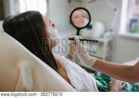Hands Of Cosmetology Specialist Applying White Facial Mask Using Brush. Making Skin Hydrated And Fac
