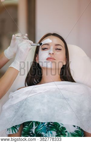 Hands Of Cosmetology Specialist Applying White Facial Mask Using Brush. Making Skin Hydrated And Fac