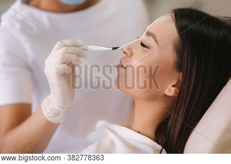 Hands Of Cosmetology Specialist Applying White Facial Mask Using Brush. Making Skin Hydrated And Fac
