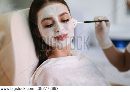 Hands Of Cosmetology Specialist Applying White Facial Mask Using Brush. Making Skin Hydrated And Fac