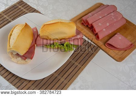 Mortadella And Lettuce Sandwich On A White Plate On A Mat And Slices Of Mortadella On The Side On A