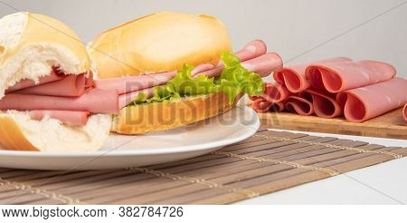 Mortadella Sandwich And Lettuce On A White Plate On A Mat And Slices Of Mortadella Next To It On A C