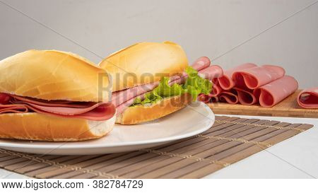 Mortadella Sandwich And Lettuce On A White Plate On A Mat And Slices Of Mortadella Next To It On A C