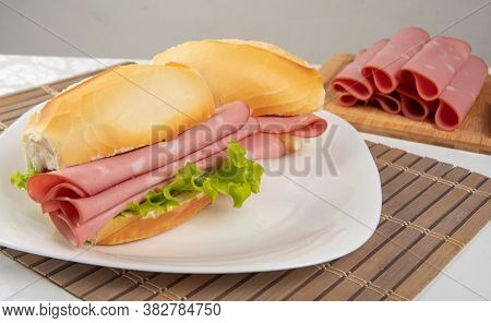 Mortadella Sandwich And Lettuce On A White Plate On A Mat And Slices Of Mortadella Next To It On A C