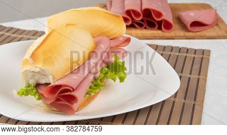 Mortadella Sandwich And Lettuce On A White Plate On A Mat And Slices Of Mortadella Next To It On A C