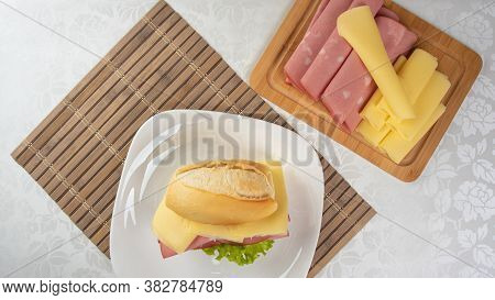 Mortadella Sandwich, Lettuce And Cheese On A White Plate On A Mat And Slices Of Mortadella And Chees