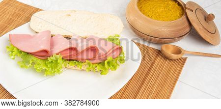 Mortadella And Lettuce Sandwich, On A White Plate And A Bamboo Mat And Pepper Sauce And Mustard On A