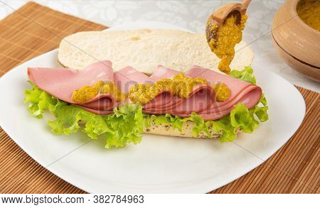 Mortadella And Lettuce Sandwich, On A White Plate And A Bamboo Mat And Pepper Sauce And Mustard On A