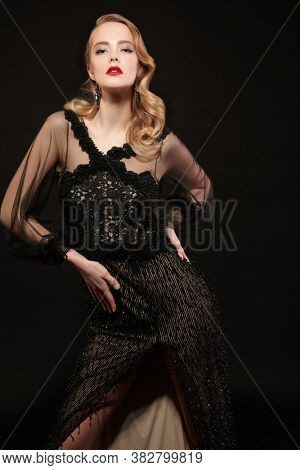 Portrait of a beautiful woman in an elegant evening dress on a black background. Clothing, makeup and hairstyle in the style of the 1920s.