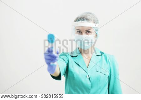 Female Doctor Or Nurse In Protective Mask At Hospital Holds Pyrometer In Hand