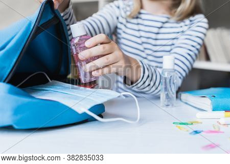 Little Girl Packing Blue Backpack In Kids's Room. Face Mask, Bottle Of Sanitizer, Stationery, Pens,