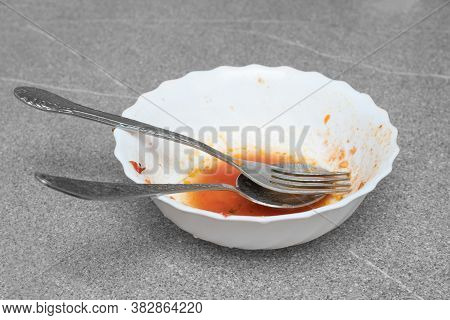 Close-up Fork And Spoon Lie In A White Dirty Plate, Gray Background, Copy Space. Dirty Dishes After 
