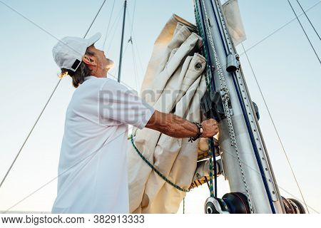 Mature Captain Looking Up While Adjusting Sail. Senior Yachtsman Preparing A Boat For A Vacation Tri