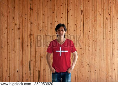 Man Wearing Denmark Flag Color Shirt And Standing With Two Hands In Pant Pockets On The Wooden Wall 