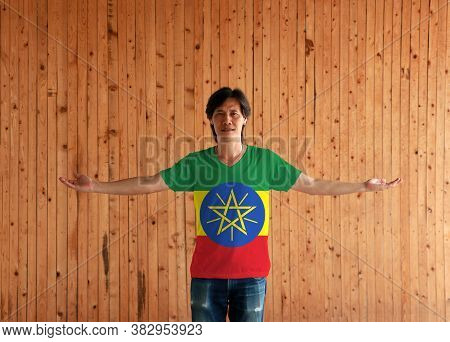 Man Wearing Ethiopia Flag Color Shirt And Standing With Arms Wide Open On The Wooden Wall Background