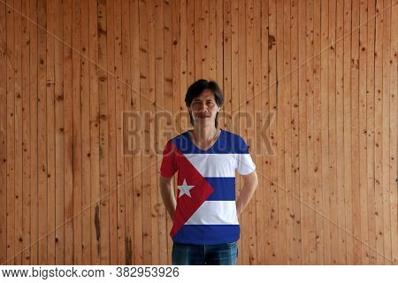 Man Wearing Cuba Flag Color Of Shirt And Standing With Crossed Behind The Back Hands On The Wooden W