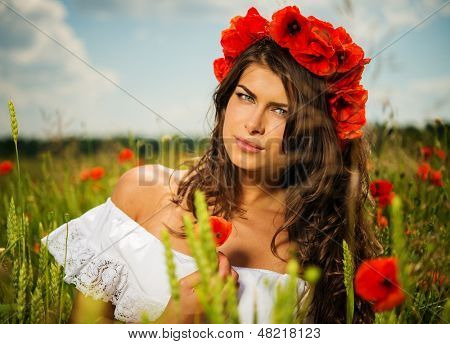 Hermosa chica morena joven vistiendo de blanco verano vestido y coronilla en amapola presentó la flor
