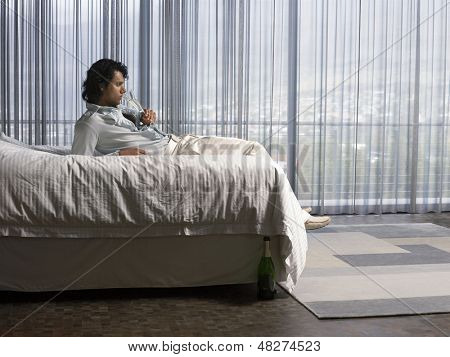 Vista laterale di un giovane uomo sorseggiando champagne nel letto 