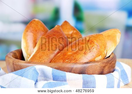 Empanadillas al horno frescos, en un recipiente de madera, en la mesa de madera, sobre fondo brillante