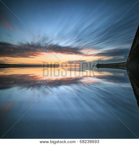 Beautiful Vibrant Sunrise Sky Over Calm Water Ocean With Lighthouse And Harbor Wall