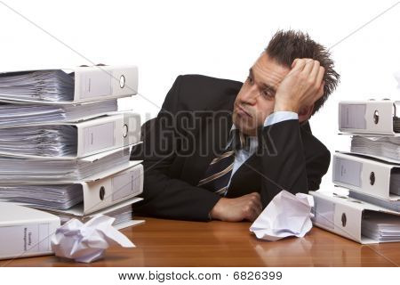 betonte Geschäftsmann sitzend frustriert zwischen Ordner Stacks in office