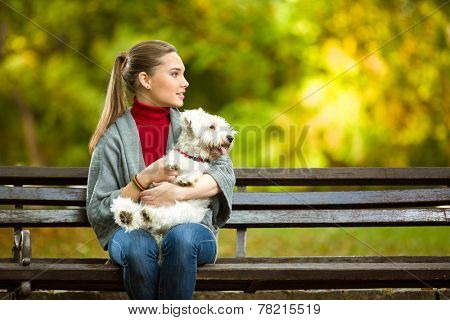 young woman hugging a maltese dog out in the park
