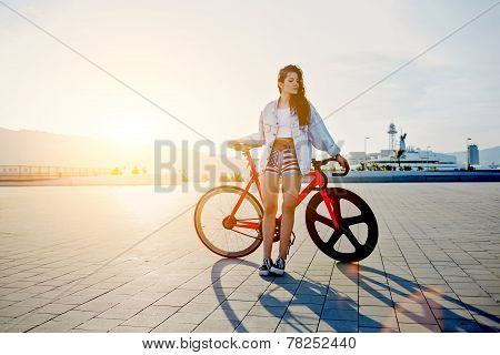 Attractive young woman win fixed gear bike posing outdoors with soft sunset light on background