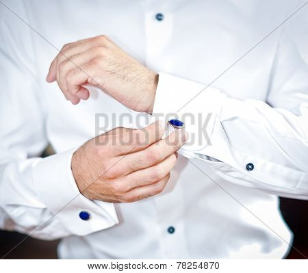 Man wears cuff-links on a shirt sleeve. A groom putting on cuff-links as he gets dressed formal wear