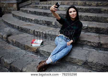 Smiling student girl making a self portrait with smart phone sitting on steps