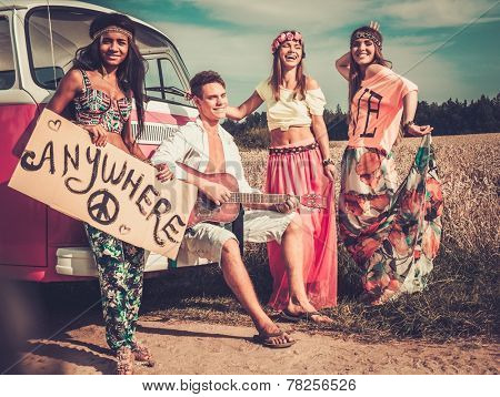 Multi-ethnic hippie hitchhikers with guitar and luggage on a road
