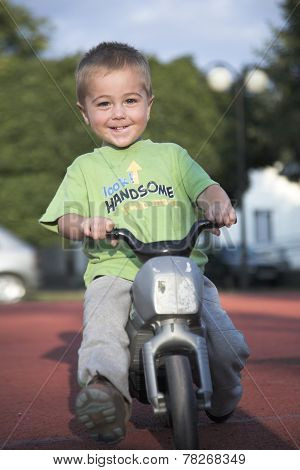 Handsome little boy rides toy motorbike, outdoor