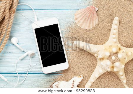 Smartphone on wood and sea sand with starfish and shells. Top view with copy space