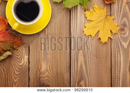Autumn leaves and coffee cup over wood background with copy space