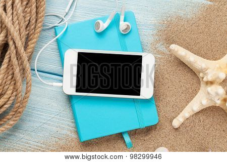 Smartphone and notepad on sea sand with starfish. Top view with copy space