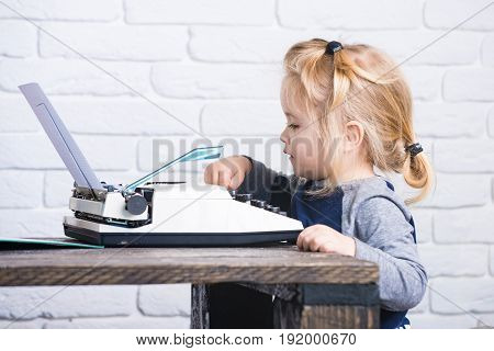 Small Boy Sitting At Table And Typing Typewriter With Paper