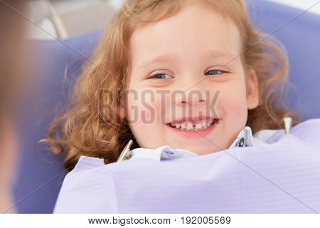 Hands of unrecognizable pediatric dentist making examination procedure for smiling cute little girl sitting on chair in hospital. Dentist office. Little girl sitting in the dentists office