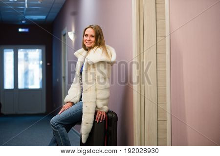 Pretty Young Blonde Woman Traveling Wearing a coat, jeans pulling a suit case.