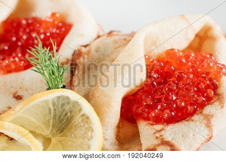 Delicacy pancakes with red caviar closeup on white plate. Russian traditional salty crepes with seafood. Shrove tuesday holiday food