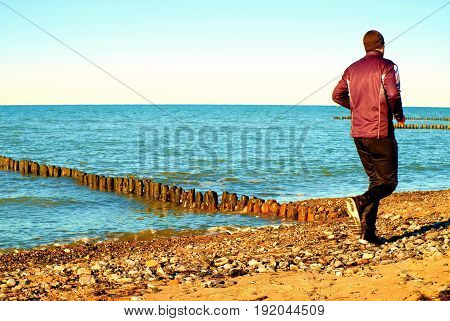 Tall Man In Dark Sportswer Running And Exercising On Stony Beach At Breakwater.