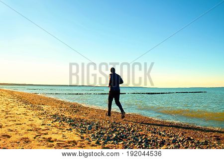 Tall Man In Dark Sportswer Running And Exercising On Stony Beach At Breakwater.