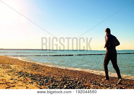 Tall Man In Dark Sportswer Running And Exercising On Stony Beach At Breakwater.