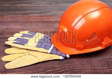 Orange hard hat and gloves for work on wood background