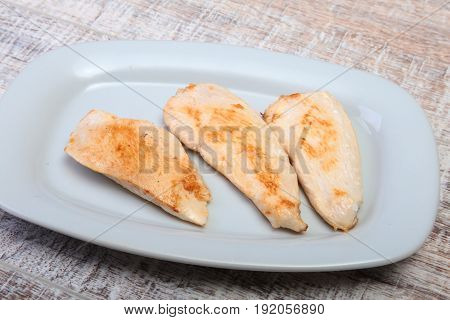 Slices of roasted chicken breast and tomato on white plate.
