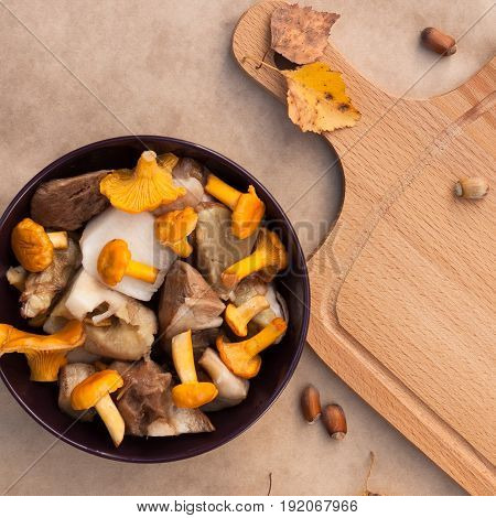 Raw Food. Bowl With Raw Cut Edible Mushrooms (Chanterelle Cep) And Cutting Wooden Board On Beige Brown Background Top View.