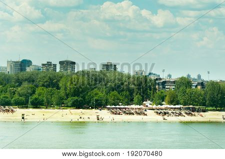 City public beach on Danube river with people, trees, buildings and cloudy sky background. Novi Sad, Serbia.
