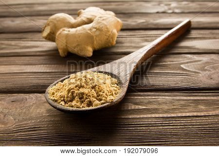 Ginger powder in wooden spoon on wooden table. Close-up. Near root of ginger