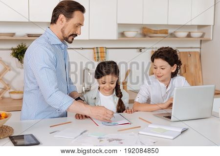 Best teacher. Handsome bearded father holding a pair of compasses and explaining a math task to his son and daughter while they listening to him attentively